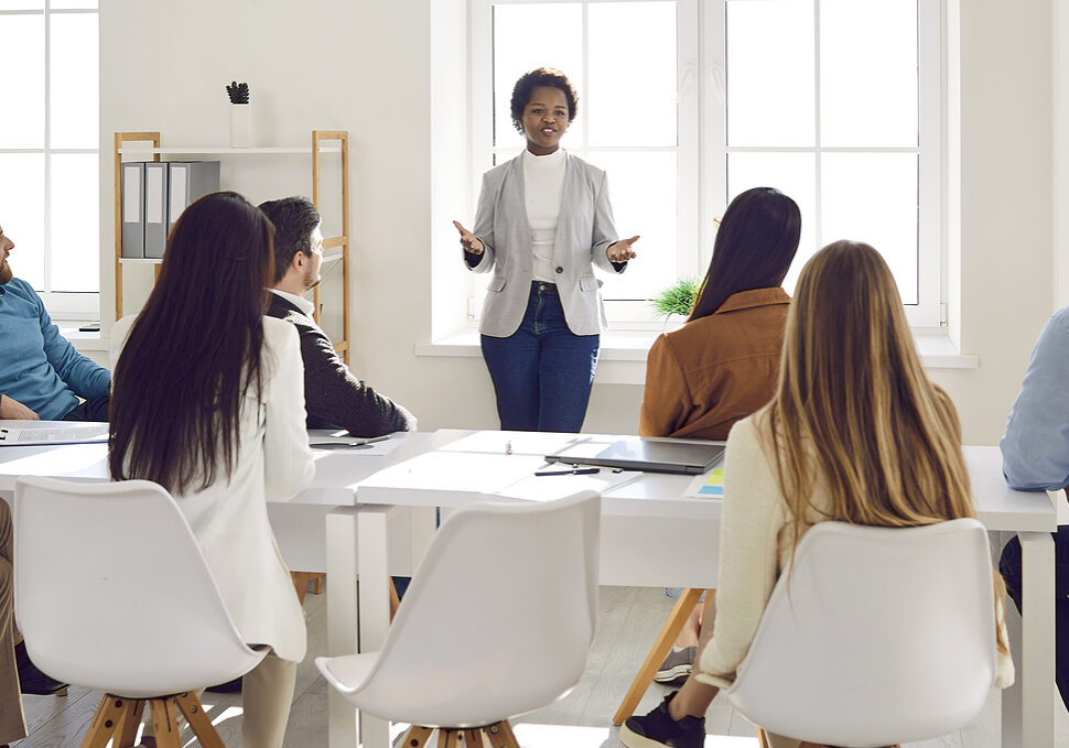 Young Black female team leader speaking to business people sitting around office table